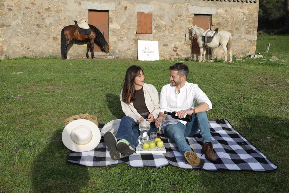 Una pareja en un pícnic frente al edificio de Finca El Sarao, con caballos al fondo