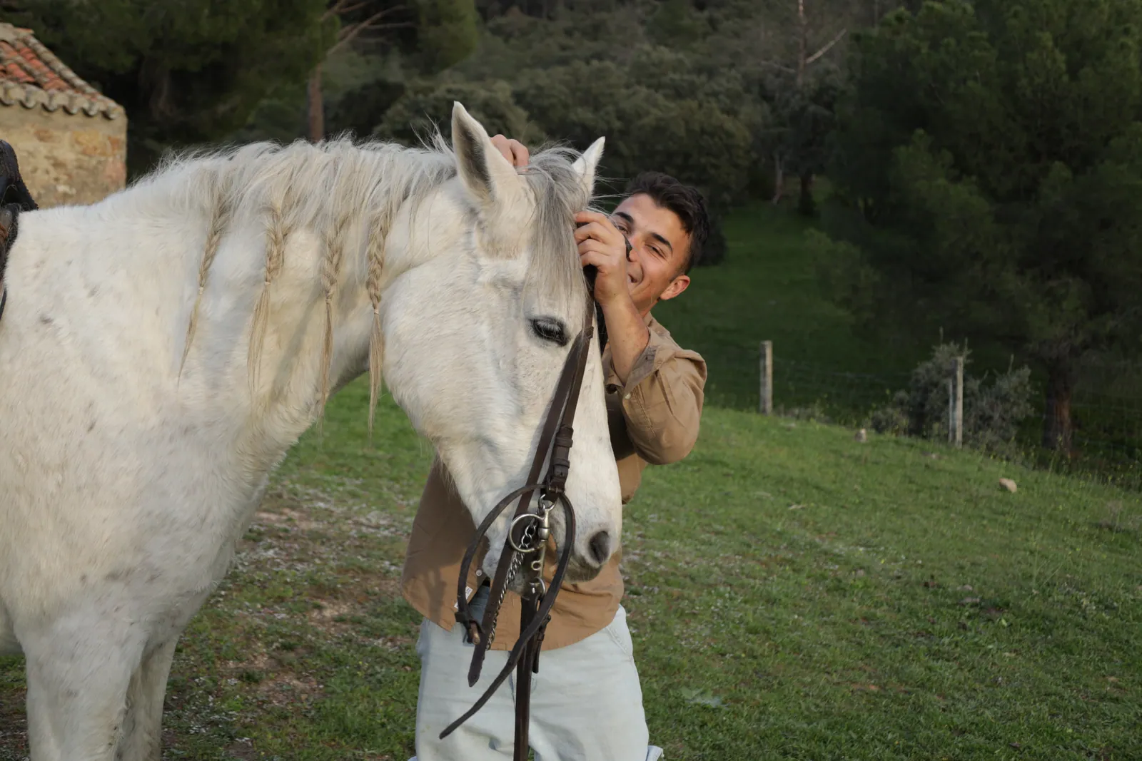 Un joven ajusta la brida de un caballo blanco junto al edificio de piedra de la finca